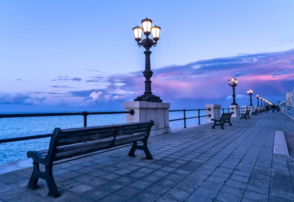 Il lungomare di Bari con panchine sull'acqua e lampioni accesi all'imbrunire.